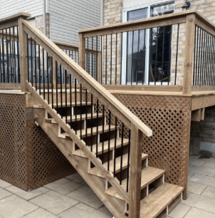 A wooden deck with railings and lattice skirting features a set of stairs leading down to a stone patio.